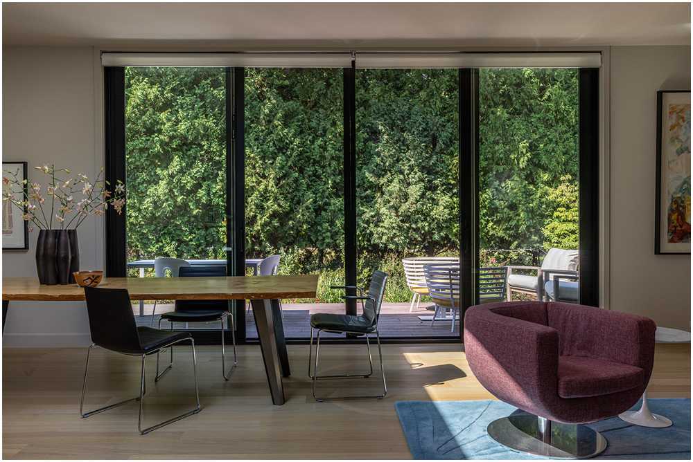 Modern dining space with large glass sliding doors, wood dining table, minimalist chairs, and view of outdoor patio — professional interiors photographer